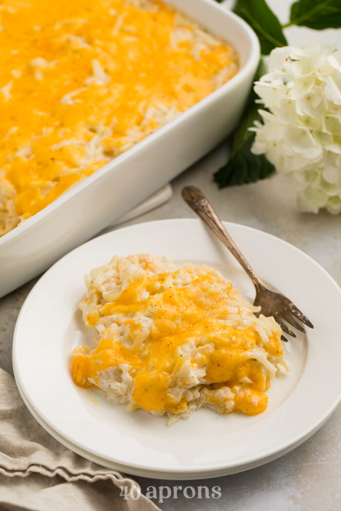 Closer, angled view of a scoop of Cracker Barrel hashbrown casserole topped with cheese on a white plate with a fork.