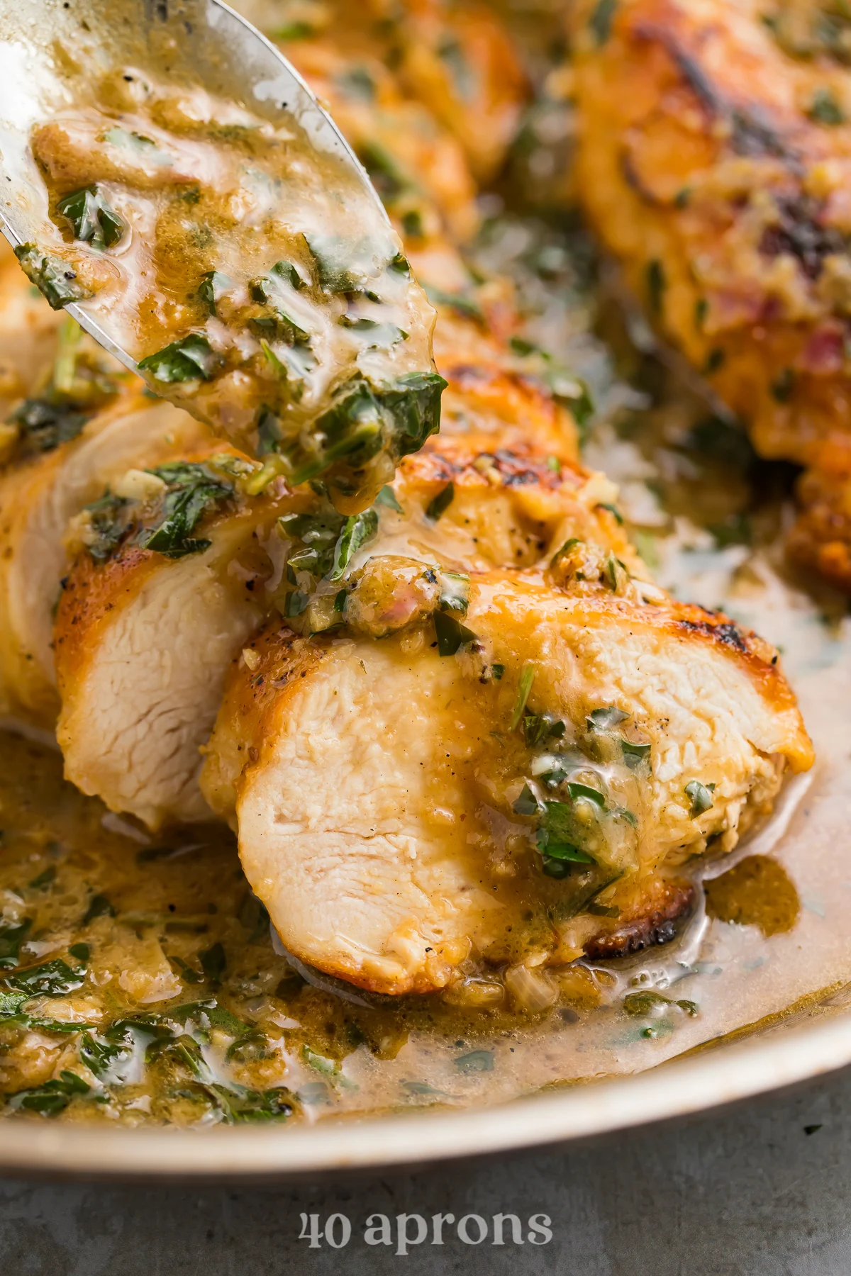 Close-up view of garlic herb butter sauce pouring from a spoon onto slices of tender chicken breast on a plate.