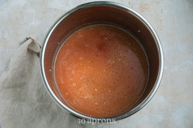 Overhead view of long grain rice, tomato sauce, chicken broth, salt, and cumin in the Instant Pot insert.