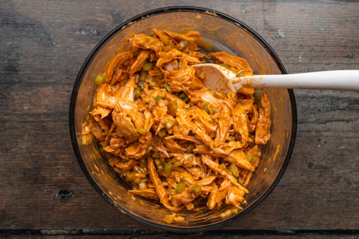 Overhead view of a bowl of buffalo chicken egg roll filling mixture with a plastic mixing spoon.