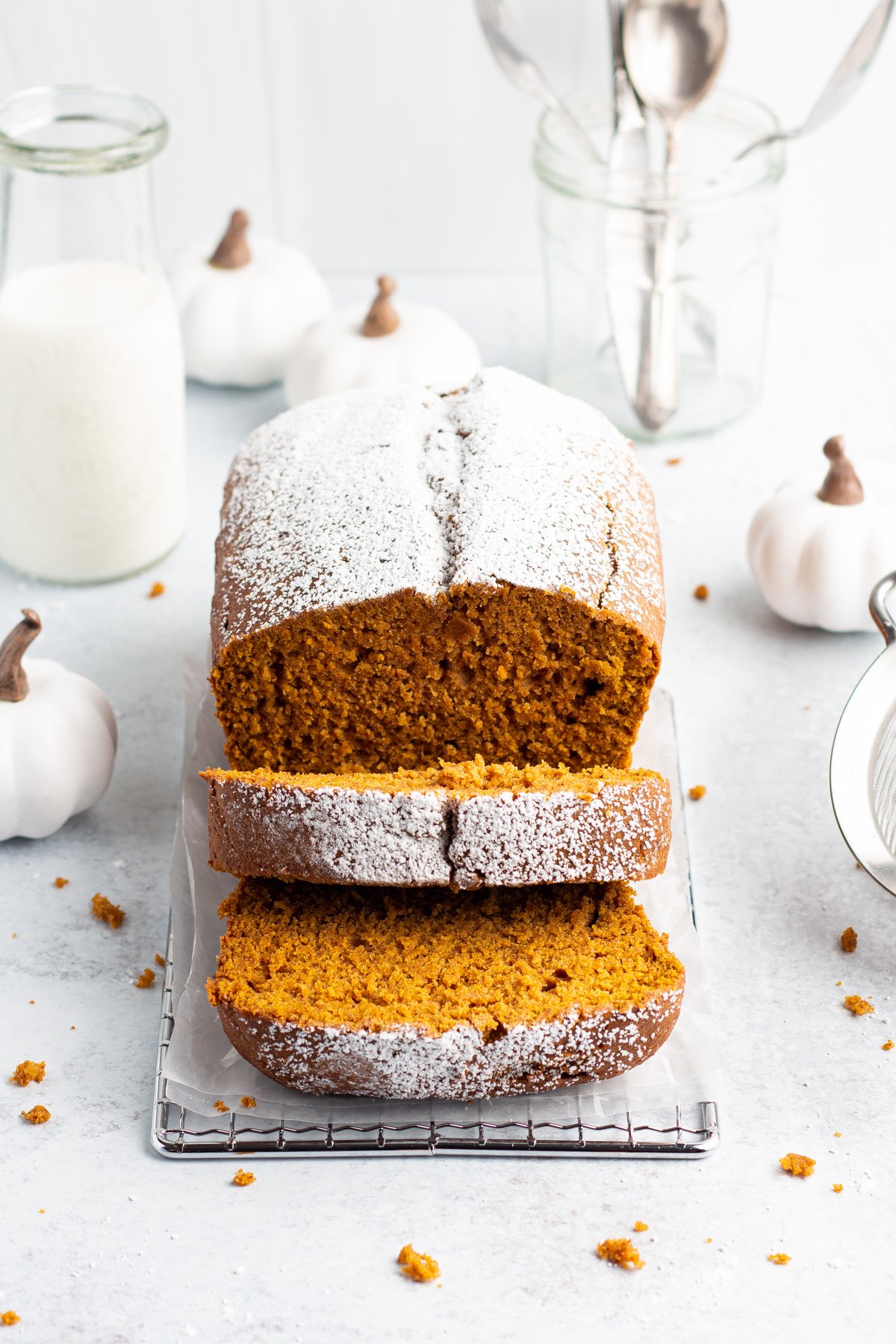 Overhead, 3/4-angle view of a loaf of gluten-free pumpkin bread topped with powdered sugar. Two slices are cut on the end of the loaf and laying on top of each other facing the viewer.