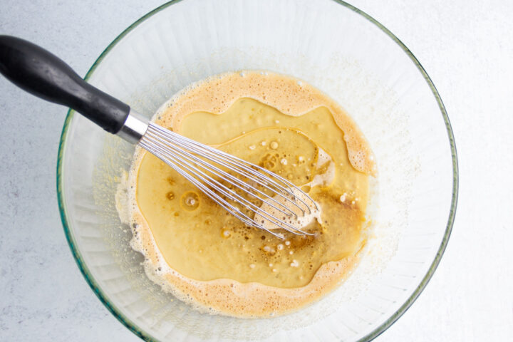 Overhead view of wet ingredients with milk in a large glass mixing bowl with a whisk.