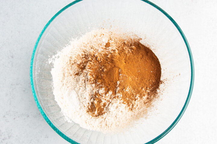 Overhead view of dry ingredients for gluten-free pumpkin bread in a large glass mixing bowl with a wooden-handled whisk.