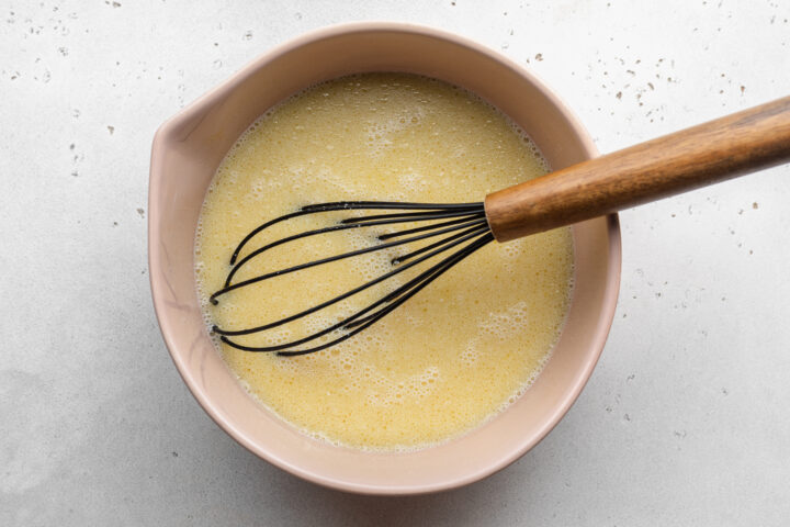 Overhead view of wet ingredients for gluten-free waffles in a large glass mixing bowl with a silicone spatula.