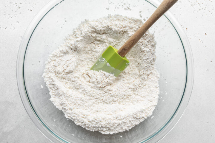 Overhead view of dry ingredients for gluten-free waffles in a large glass mixing bowl with a silicone spatula.