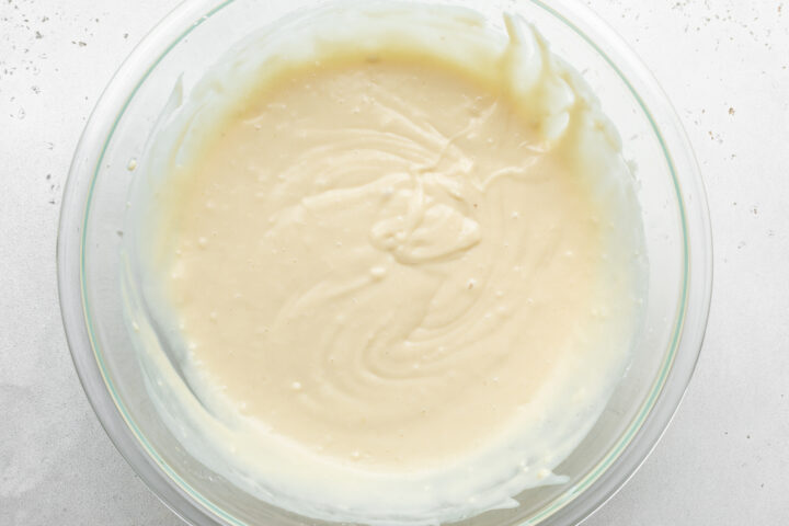 Overhead view of prepared waffle batter in a large glass mixing bowl on a white countertop.