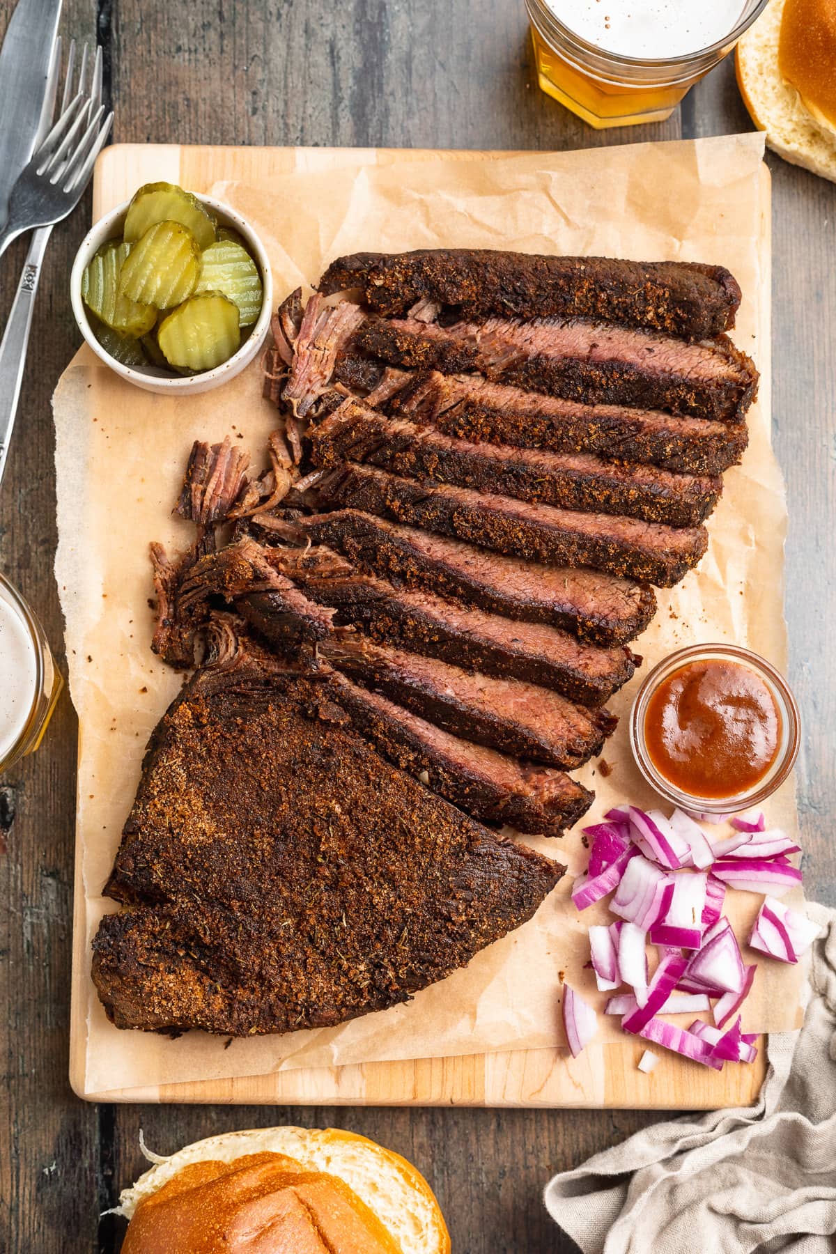 Sous vide brisket, sliced thin and arranged on a wooden serving tray with seasoning and garnish.