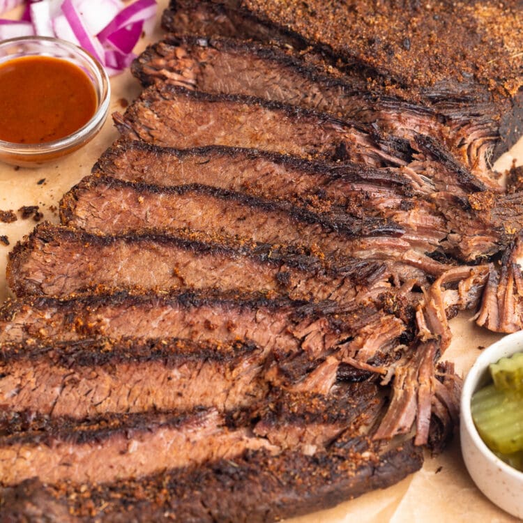 Sous vide brisket, sliced thin and arranged on a wooden serving tray with seasoning and garnish.