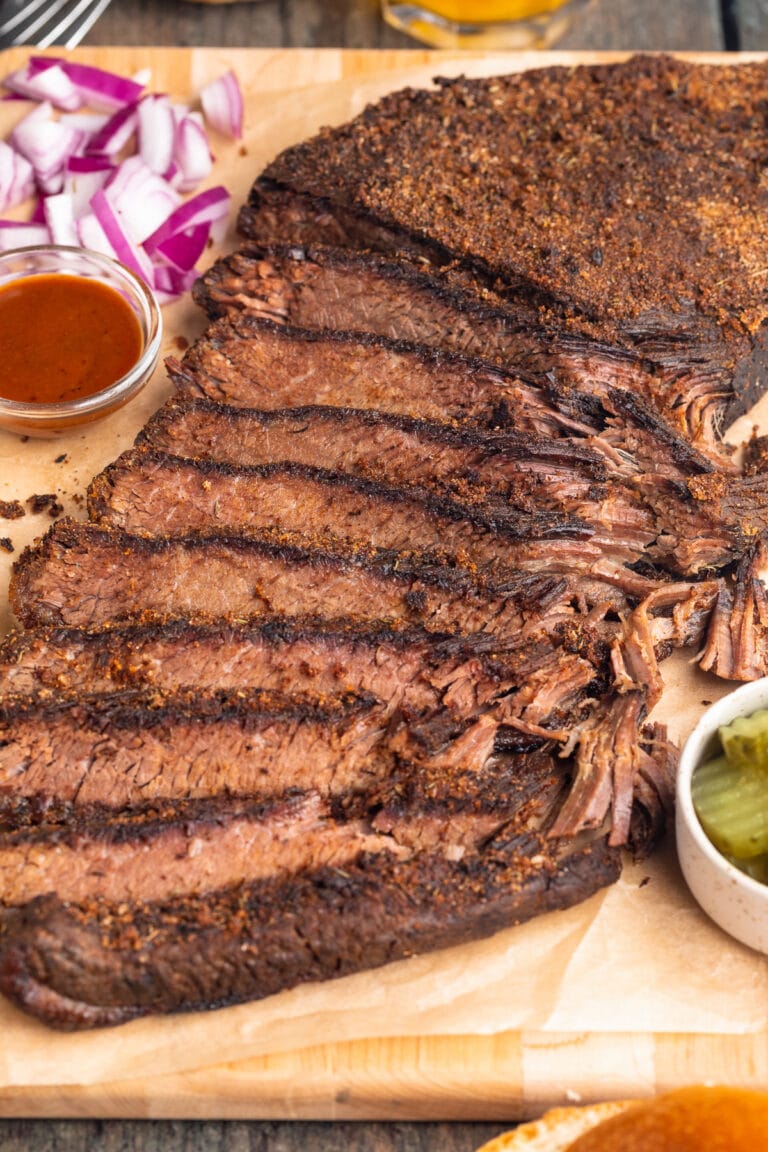 Sous vide brisket, sliced thin and arranged on a wooden serving tray with seasoning and garnish.