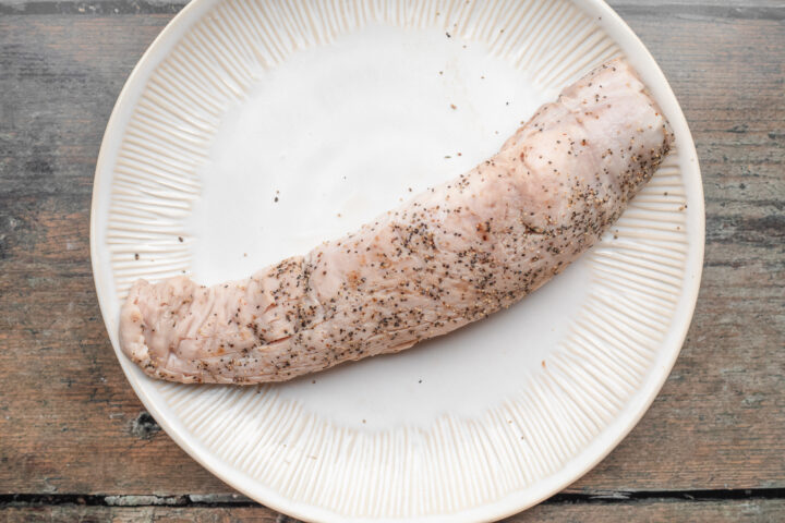 Overhead view of cooked sous vide pork tenderloin on a large white plate on a wooden table.