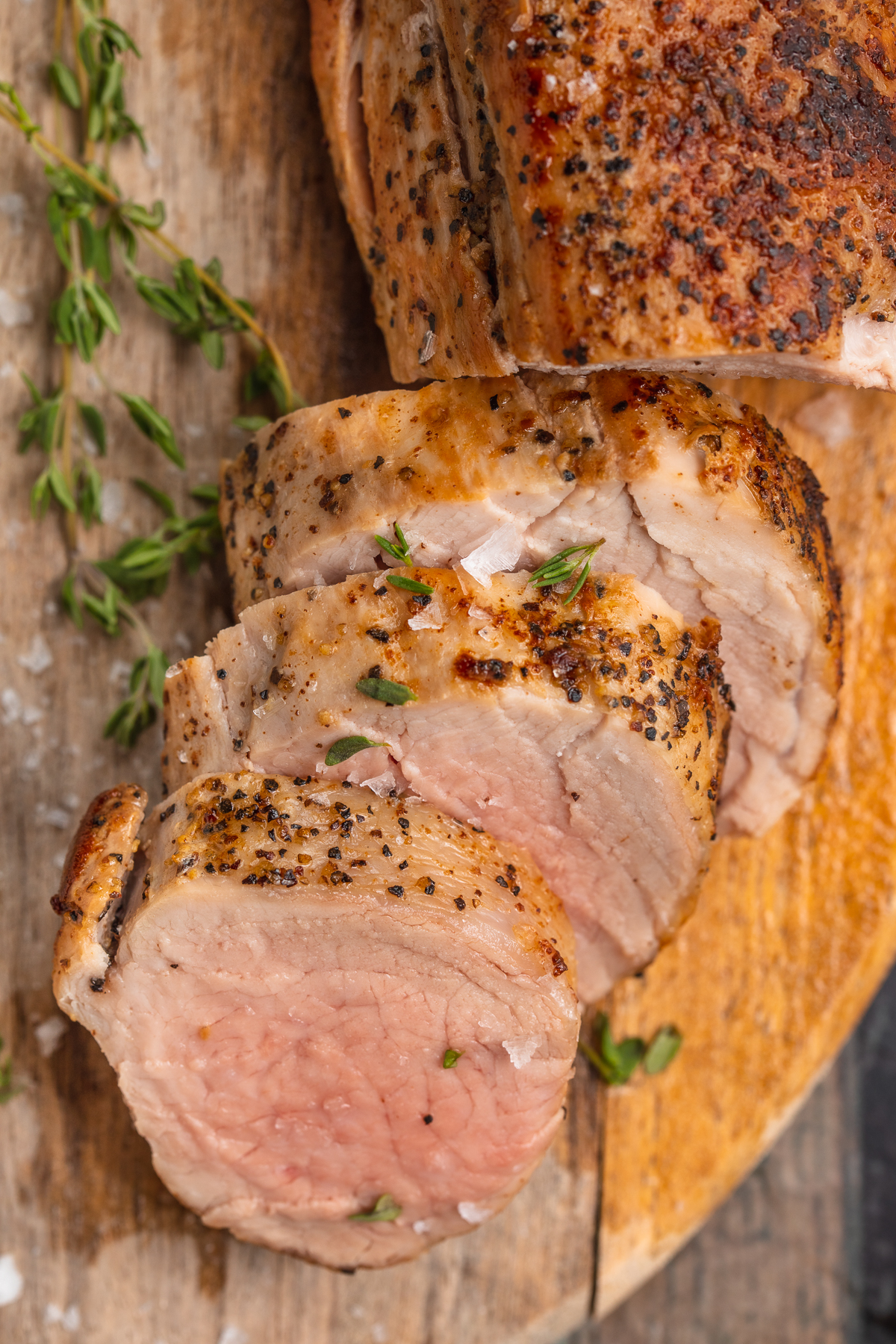 Overhead view of sous vide pork tenderloin slices on a wooden cutting board.