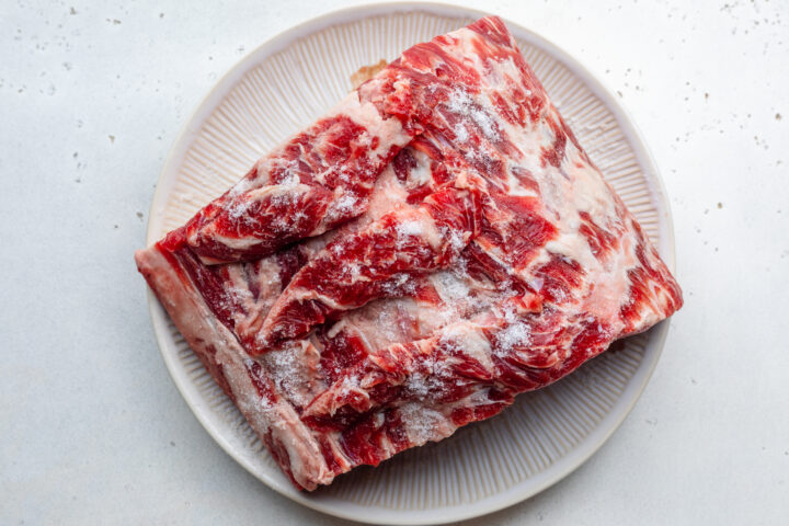 Overhead view of uncooked prime rib seasoned with salt on a round white plate.