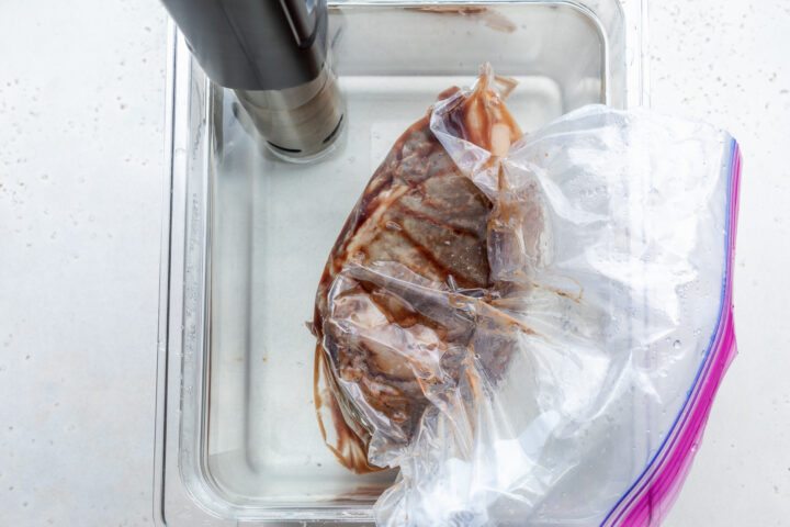 Overhead view of seasoned prime rib in a large container filled with water and a sous vide immersion circulator.