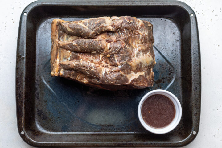 Overhead view of sous vide prime rib on a roasting pan with small ramekin of reserved juices.