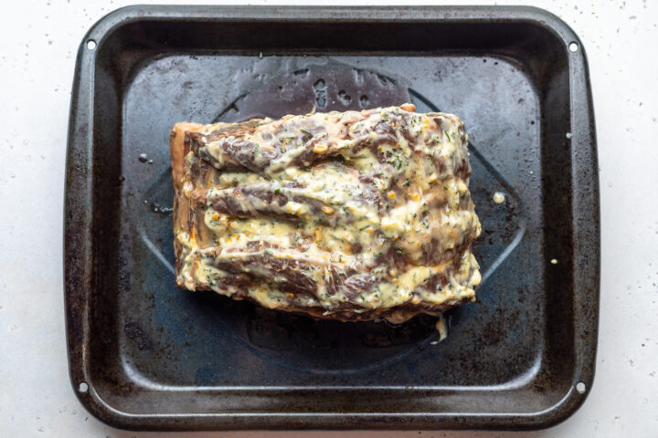 Overhead view of a sous vide prime rib rubbed with seasoned compound butter on a black roasting pan.