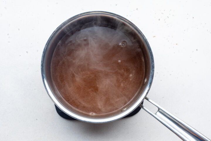 Overhead view of au jus mixture in a silver saucepan on a white countertop.