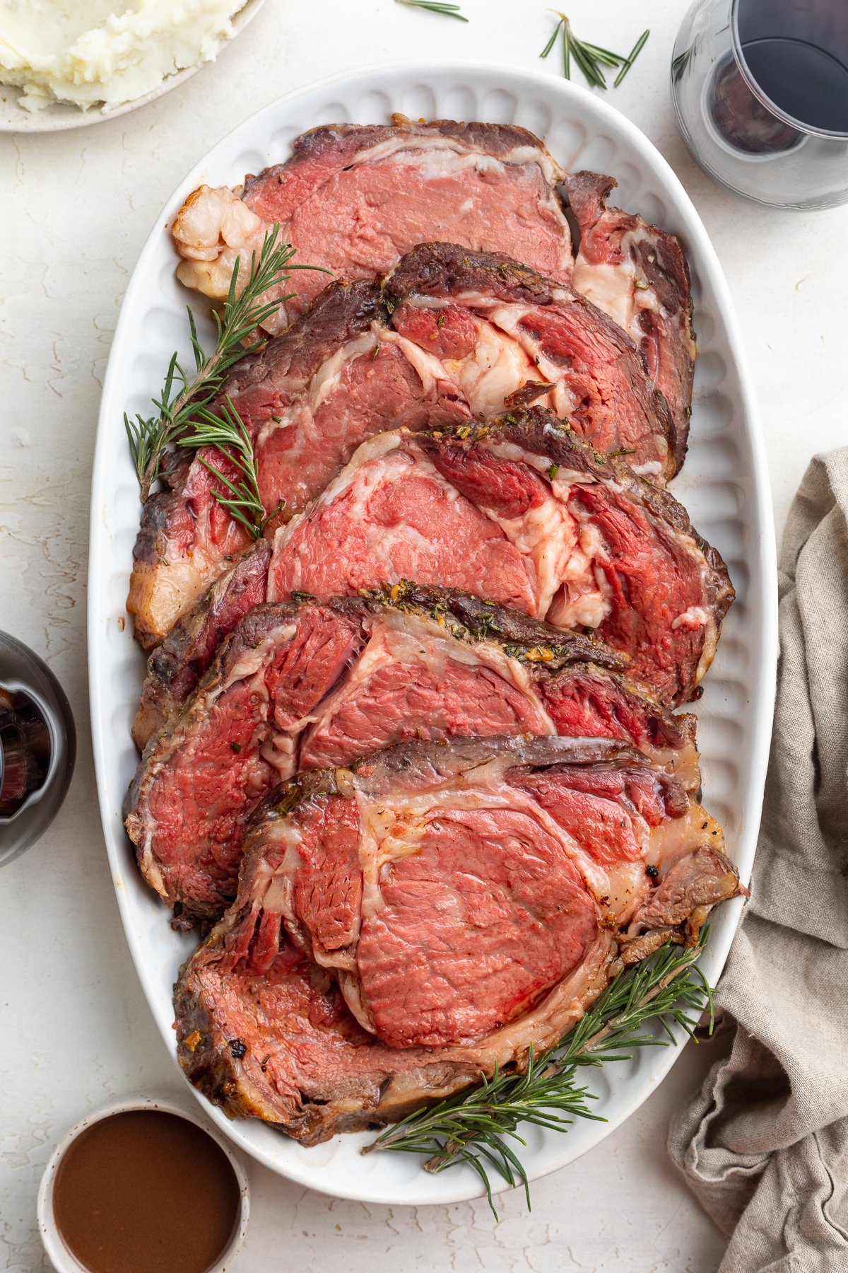 Overhead view of a platter of sliced sous vide prime rib on a white table top.