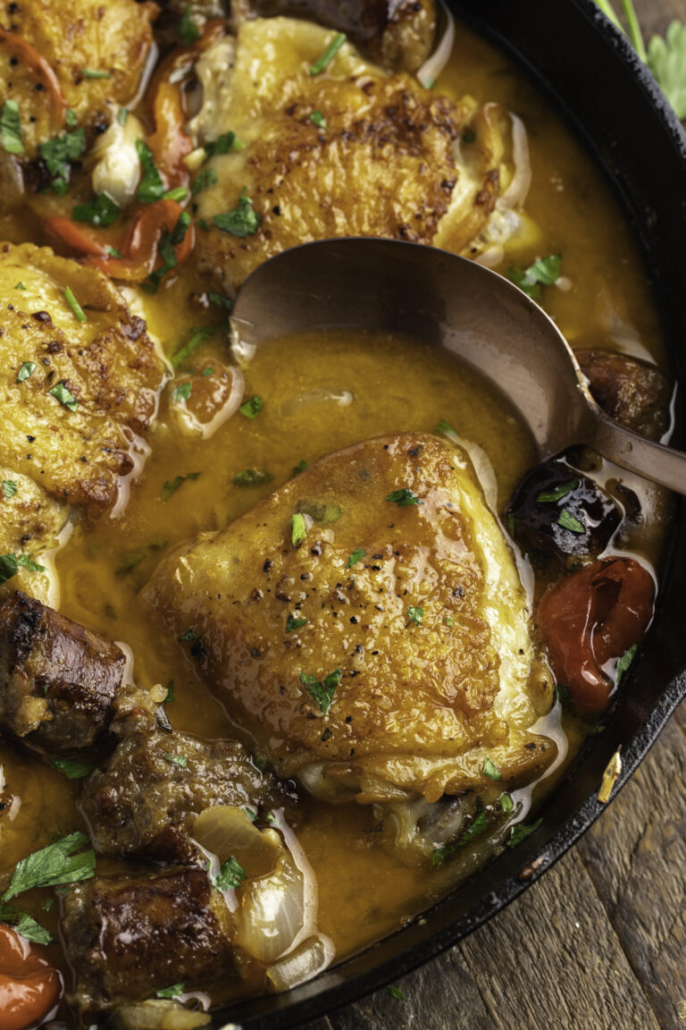 Overhead view of chicken scarpariello in a large cast iron skillet with a spoon on a wooden background.