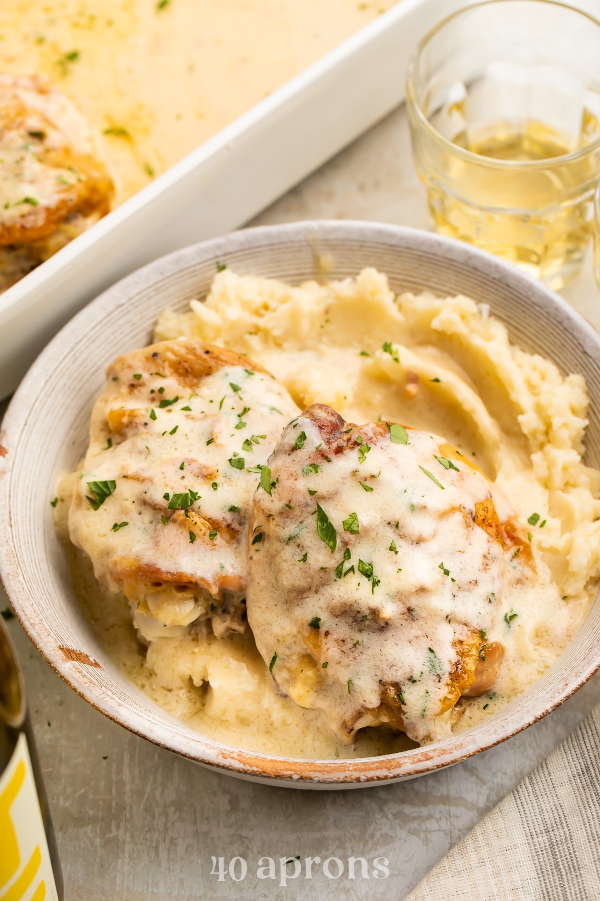 Angled view of a bowl of chicken soup chicken over a bed of creamy mashed potatoes, with a casserole dish of chicken in the background.