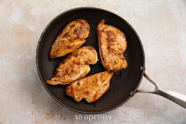 Overhead view of 4 chicken cutlets in a large cast iron skillet. Cutlets have been fried until golden brown.