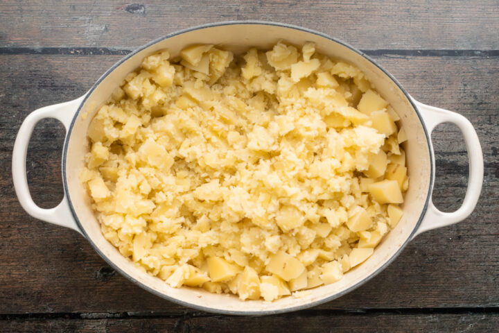 Overhead view of lightly mashed boiled potatoes in an oval baking dish with handles.