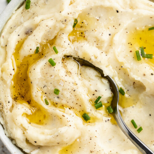 Close-up, overhead view of the left half of a large white bowl holding dairy-free mashed potatoes topped with brown gravy.