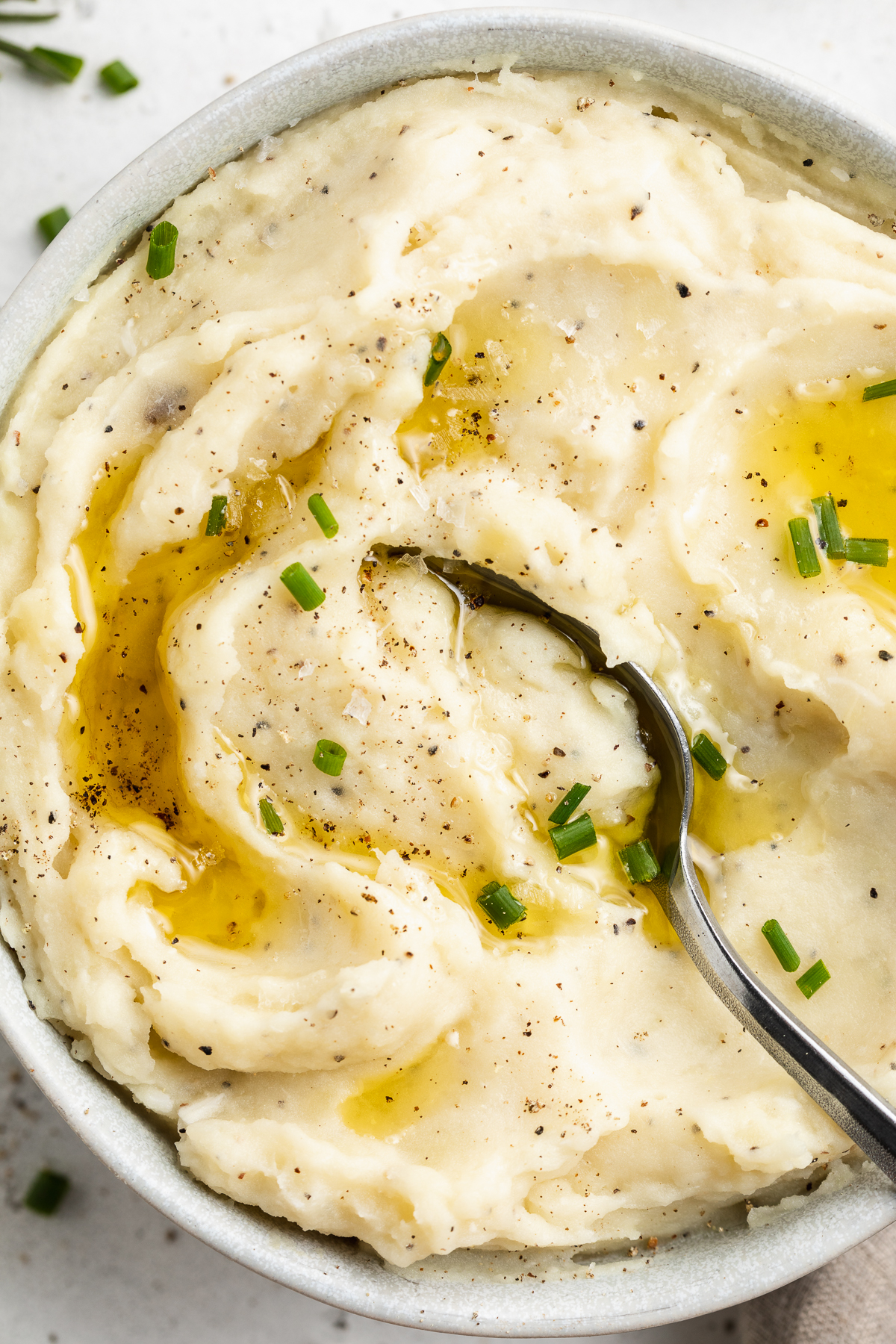 Close-up, overhead view of the left half of a large white bowl holding dairy-free mashed potatoes topped with brown gravy.