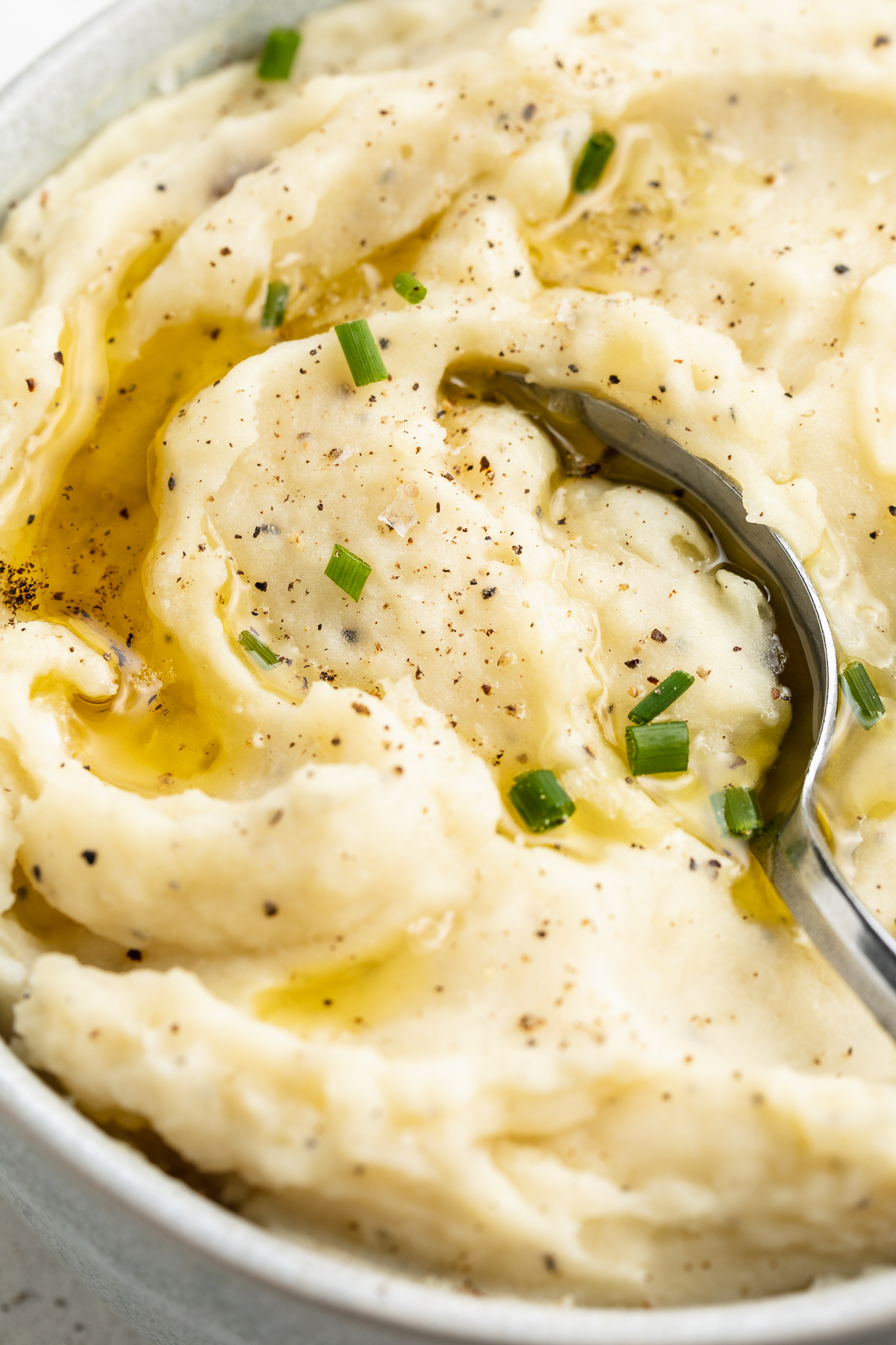 Close-up, overhead view of the left half of a large white bowl holding dairy-free mashed potatoes topped with brown gravy.