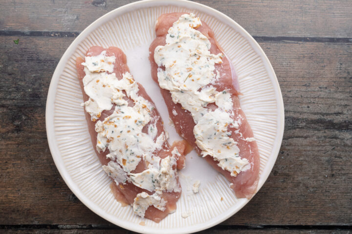 Overhead view of two turkey loins topped with a thick compound butter mixture on a white plate against a wooden countertop.