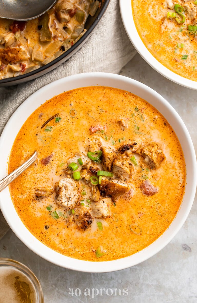 Overhead, zoomed-in view of a bowl of creamy cajun chicken soup in a white soup bowl with a silver spoon on a marble countertop.