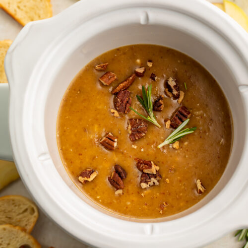 Overhead view of a small Crockpot containing a deep orange brie dip topped with chopped pecans.