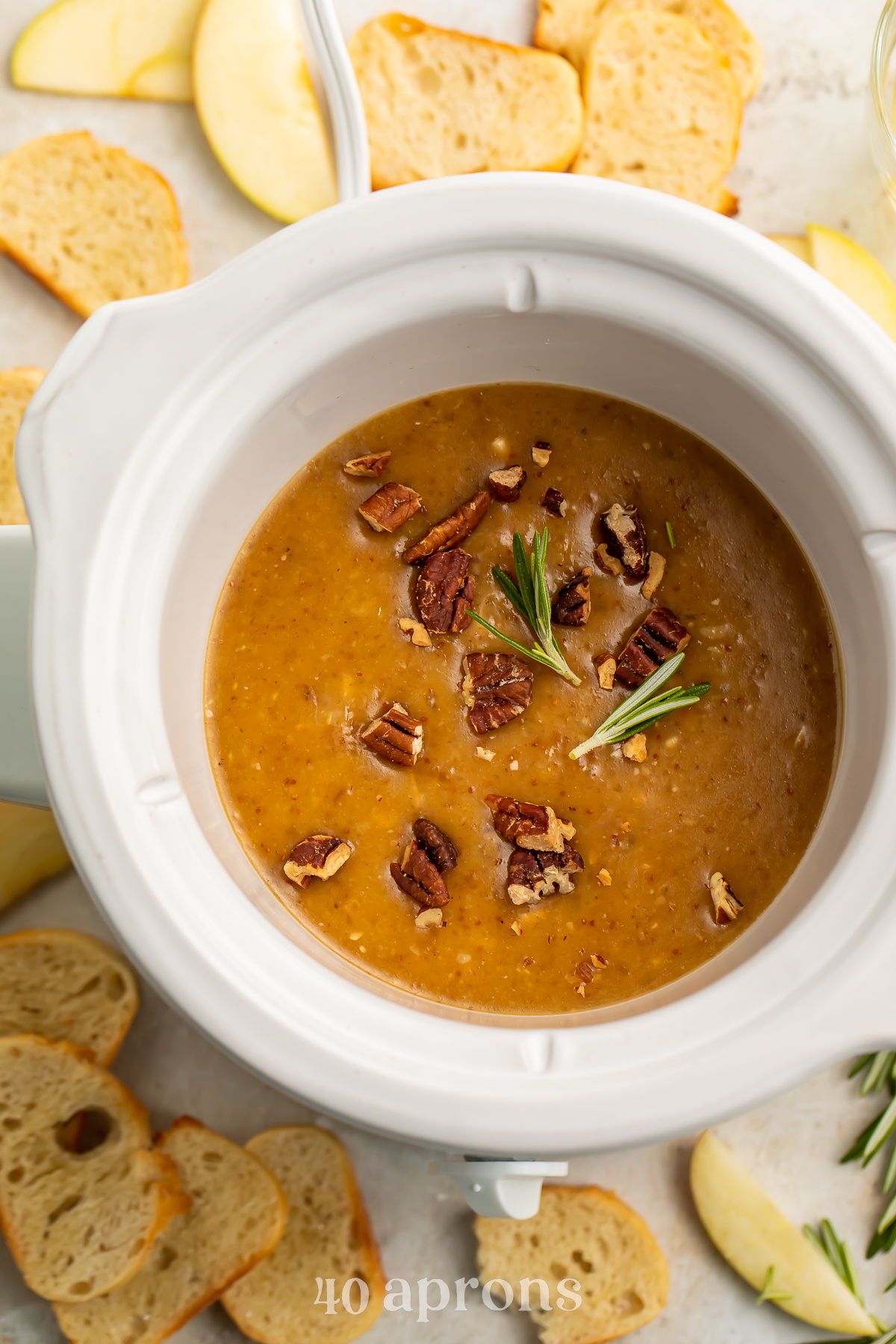 Overhead view of a small Crockpot containing a deep orange brie dip topped with chopped pecans.