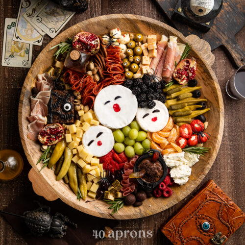 Overhead view of a Hocus Pocus themed charcuterie board with brie, fruit, cornichon, stuffed red peppers, marinated mozzarella, and other spooky snacks.