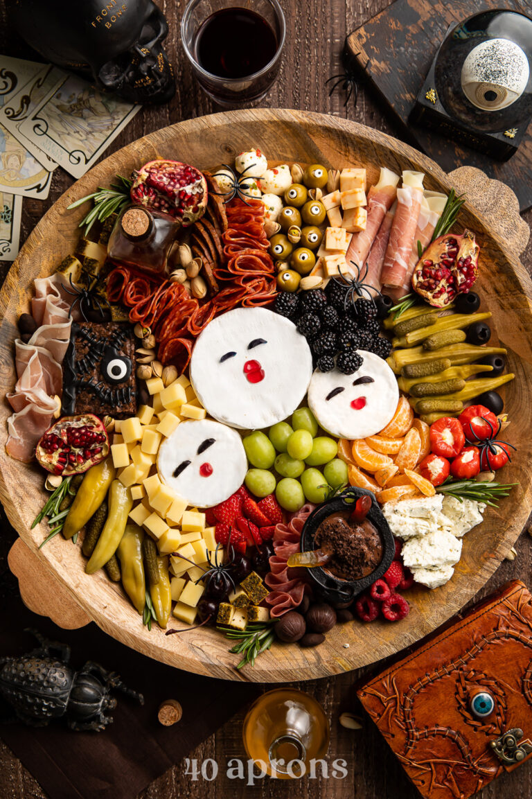 Overhead view of a Hocus Pocus themed charcuterie board with brie, fruit, cornichon, stuffed red peppers, marinated mozzarella, and other spooky snacks.