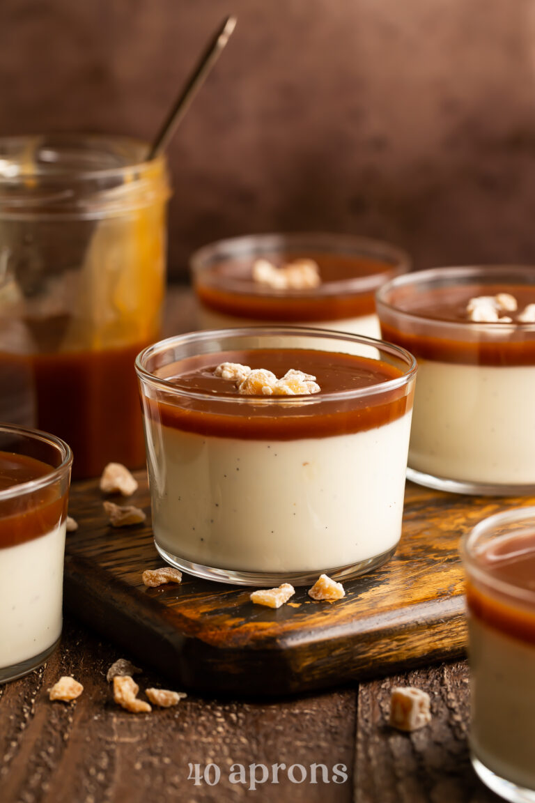 Side view of small glass pudding cups holding creamy panna cotta topped with rich caramel sauce.