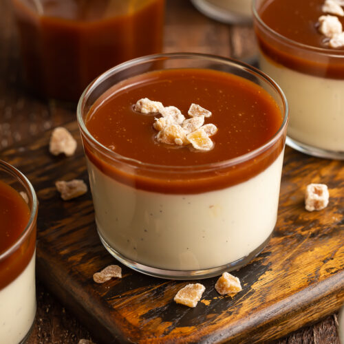 Overhead, angled view of vanilla bean panna cotta in a glass pudding cup topped with rich, dark caramel sauce.