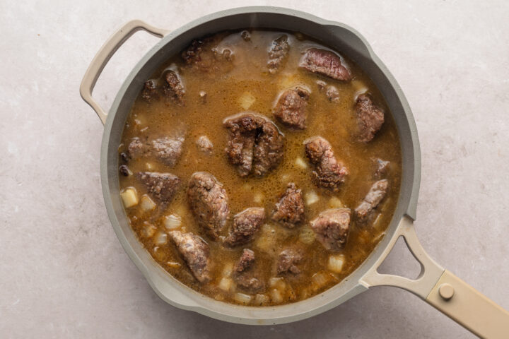 Overhead view of cooked beef tips in a pool of dark brown gravy in a large skillet.