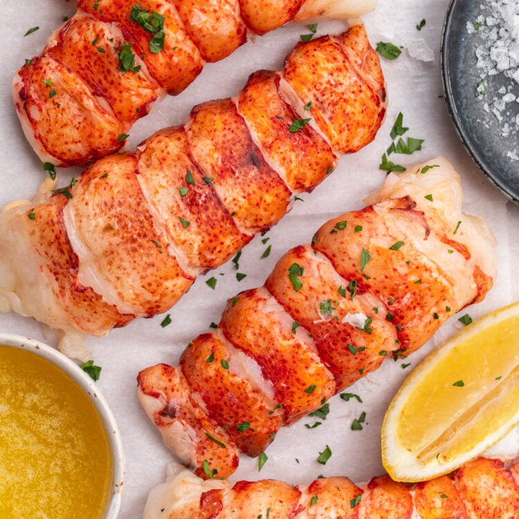 Overhead view of 4 bright red sous vide lobster tails lined up on a cutting board from the top left of the photo down to the bottom right corner.