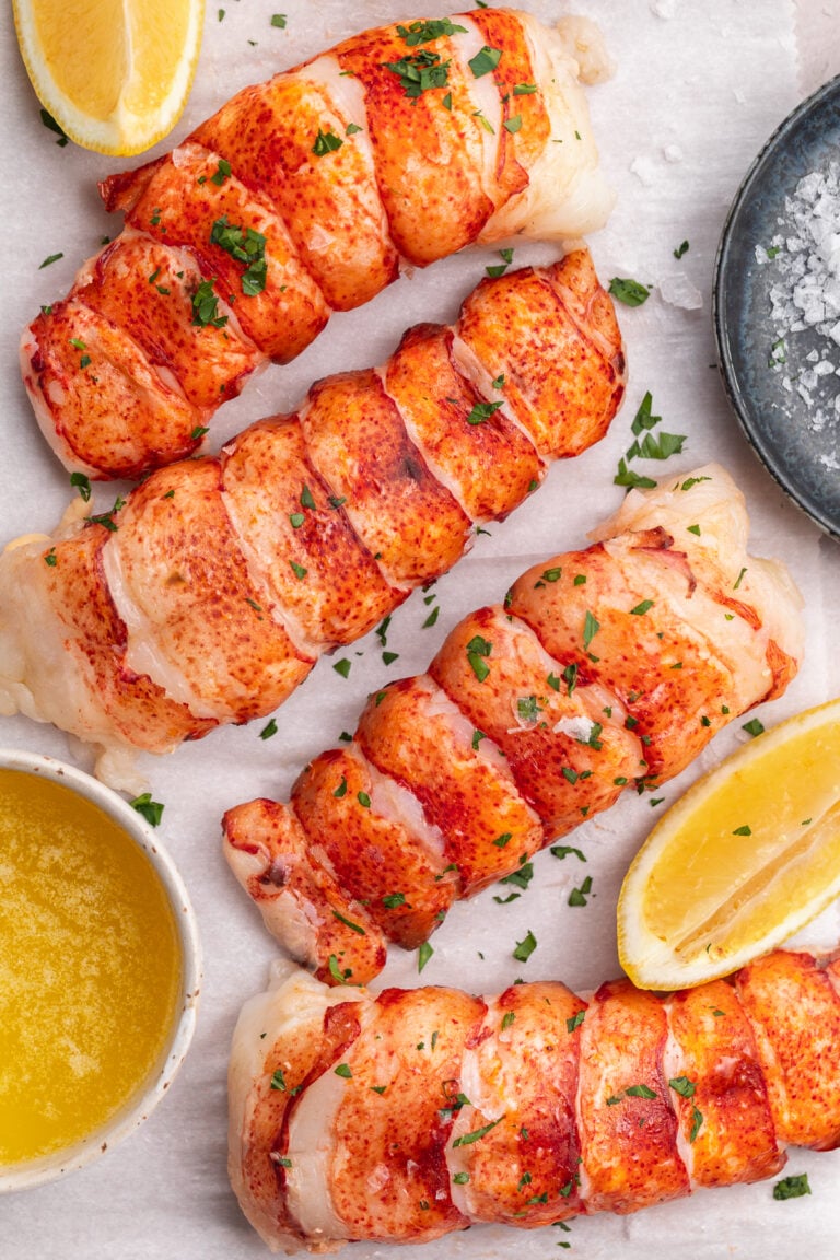 Overhead view of 4 bright red sous vide lobster tails lined up on a cutting board from the top left of the photo down to the bottom right corner.