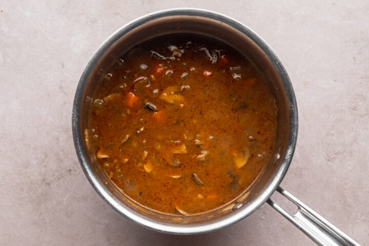 Overhead view of beef stew in a large silver saucepan.