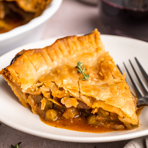 A wedge-shaped slice of beef pot pie on a white plate with a silver fork. The edge of the remaining pot pie is in the background.