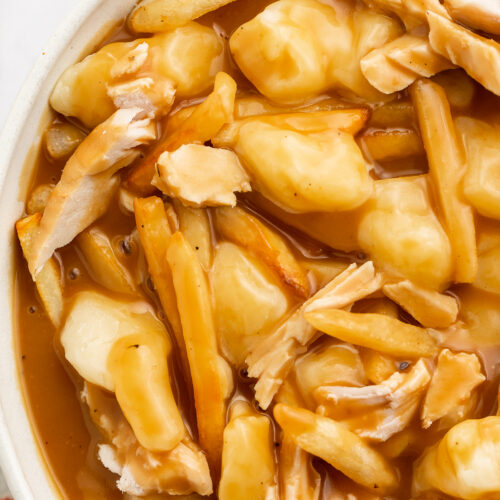 Overhead view of the left half of a large bowl of leftover turkey poutine with fries and gravy.