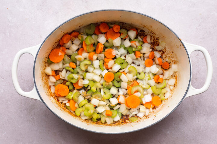 Overhead view of pork, carrots, onions, celery in a large dutch oven.