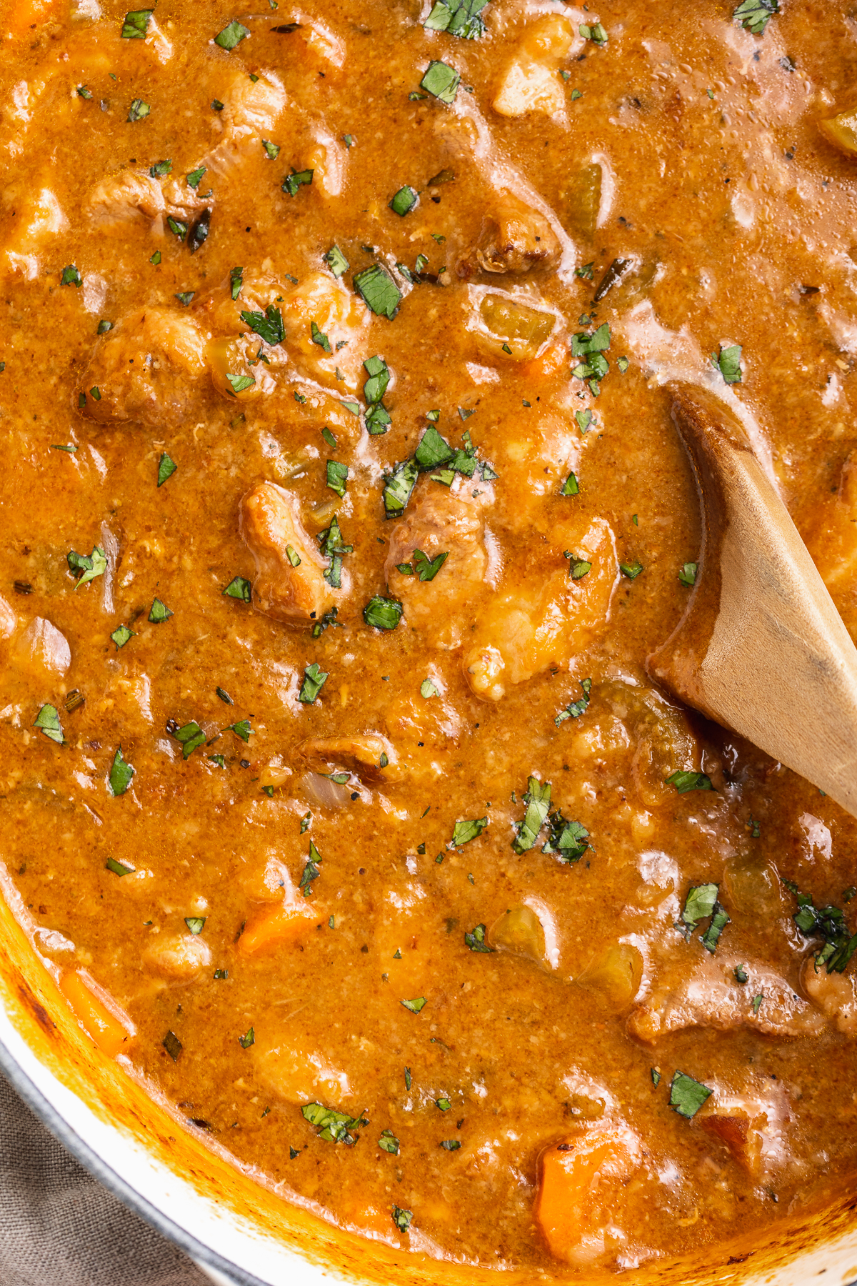 Close-up of pork stew in a large Dutch oven with a wooden spoon.