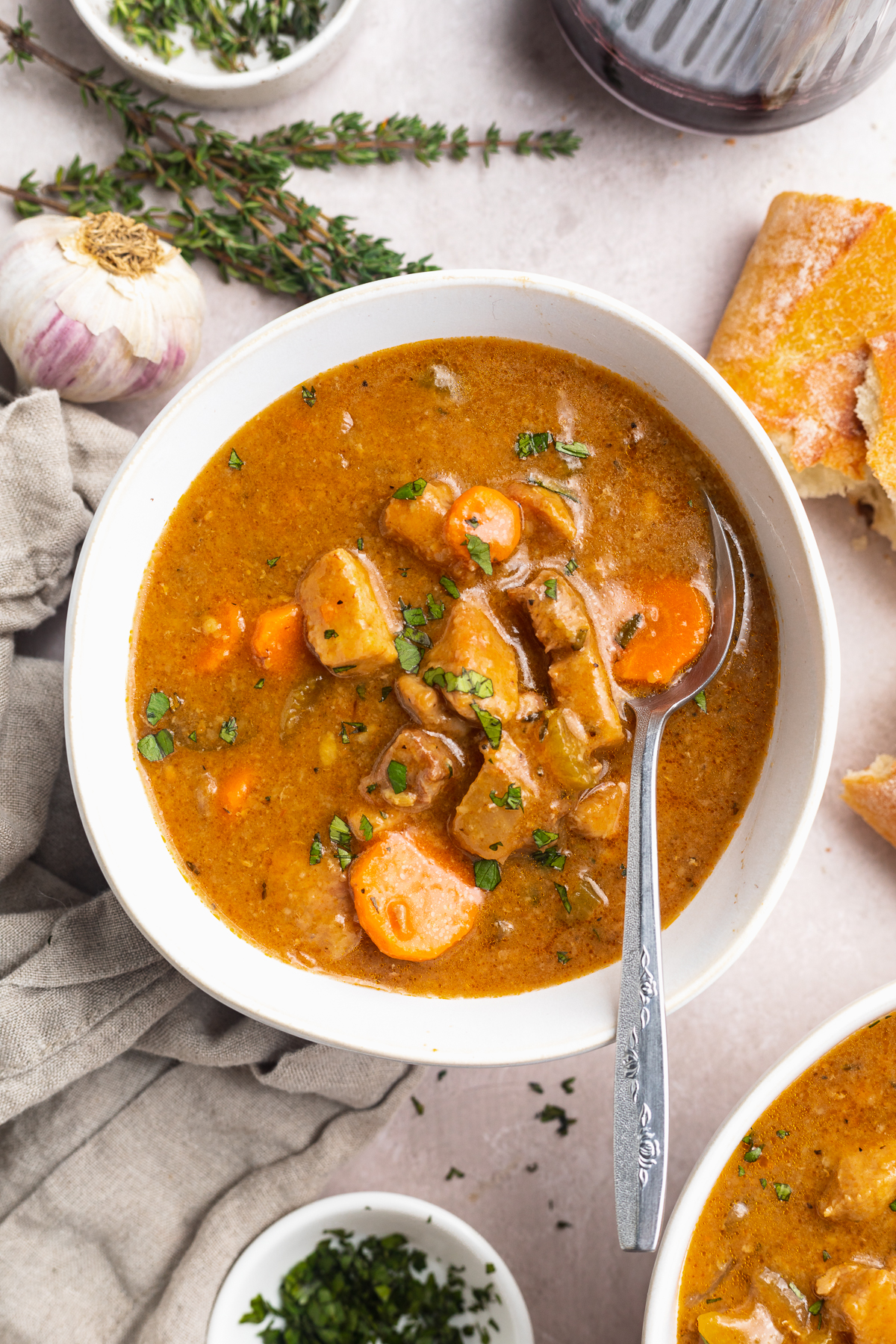 Overhead view of a bowl of pork stew on a table with recipe ingredients scattered around.