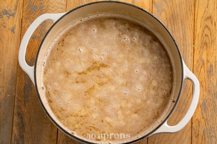 Overhead view of boiling chicken stock in a dutch oven with diced onions and minced garlic.