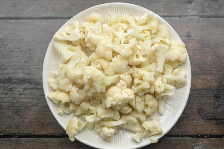 Overhead view of cauliflower florets on a large white round plate.