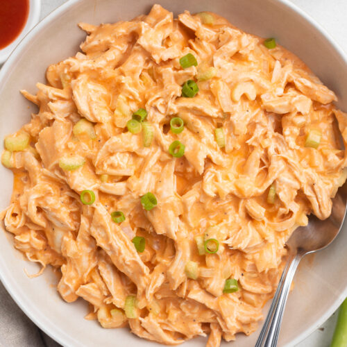 Overhead view of a bowl of Whole30 buffalo chicken salad on a neutral table. A spoon rests in the salad.