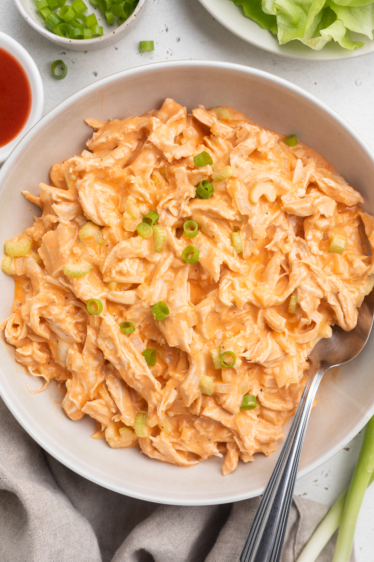 Overhead view of a bowl of Whole30 buffalo chicken salad on a neutral table. A spoon rests in the salad.