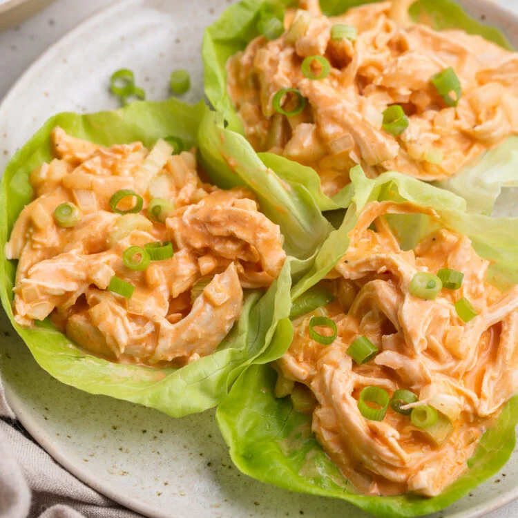 Whole30 buffalo chicken salad scooped into three iceberg lettuce cups on a white plate.